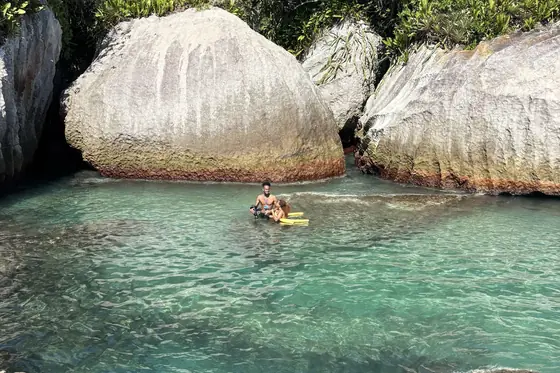 Pessoa boiando em um flutuador amarelo, entre as pedras da ilha.