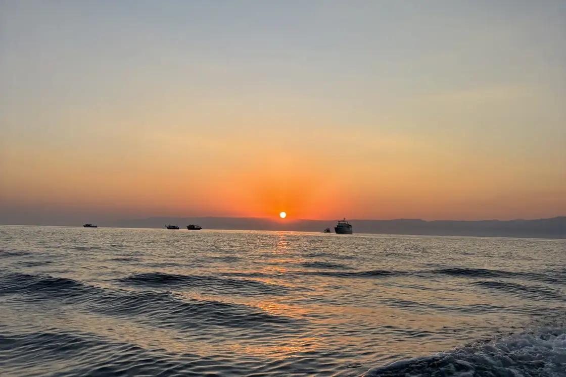 O sol baixo no horizonte do mar, com o reflexo dourado na água.