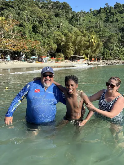 Adultos e uma criança na parte rasa, perto da praia.