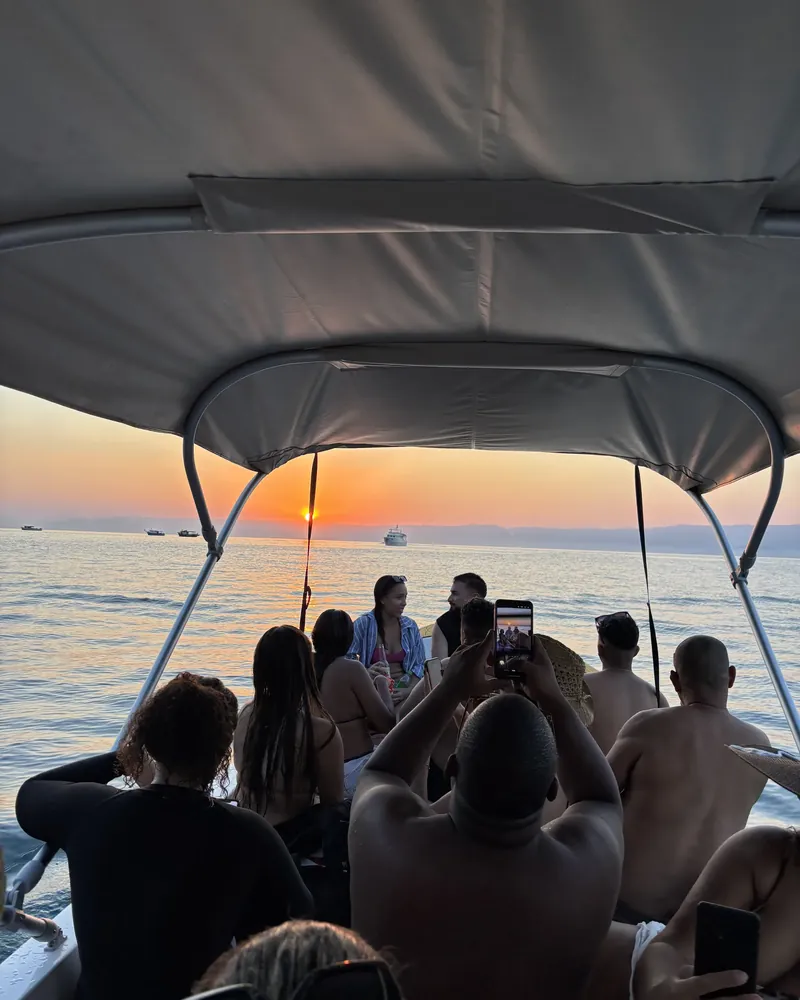 O grupo sentado sob a cobertura do barco, olhando o sol nascer no mar aberto.