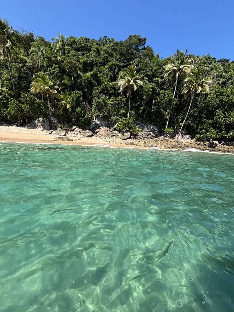 A faixa de areia d'As Ilhas, com coqueiros e a água rasa e transparente.