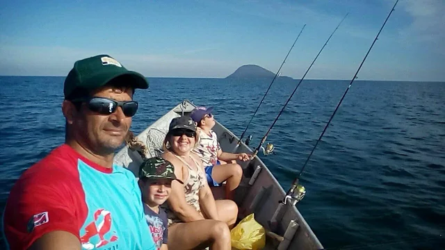Foto antiga de pescaria: uma família dentro do barco, com as varas na água e uma ilha ao fundo.