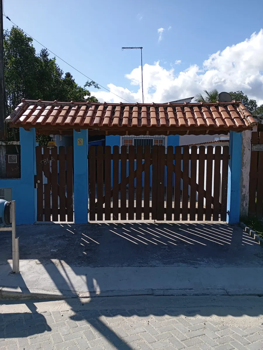 Fachada da casa, pintada de azul, com portão de madeira e telhado de telhas.