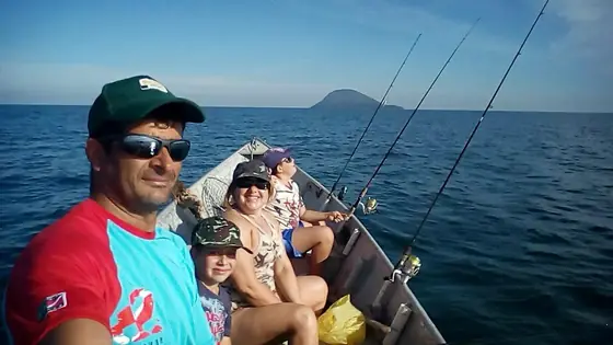 Família a bordo durante a pescaria, com o mar aberto atrás.