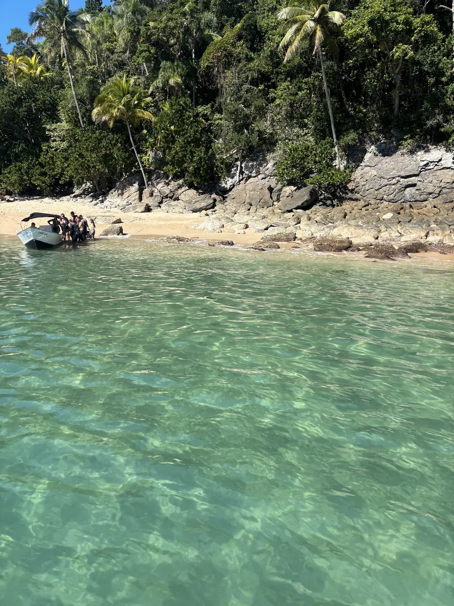 Barco fundeado na beira da praia d’As Ilhas, entre coqueiros e pedras.