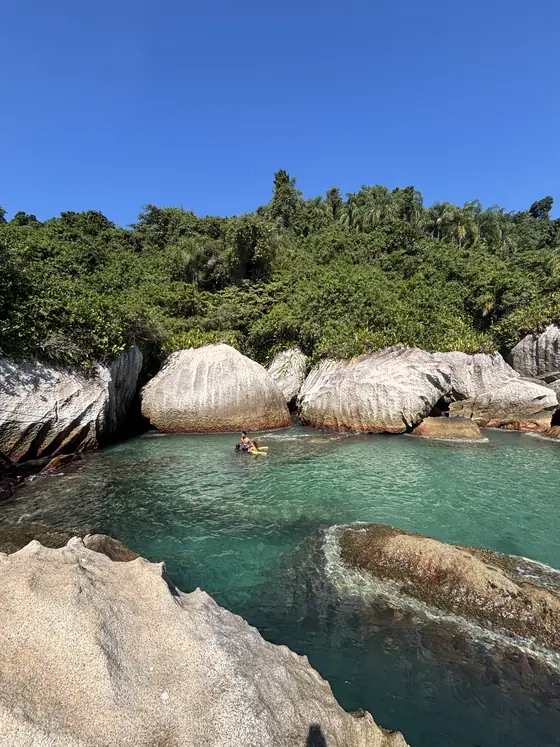 Piscina natural do Montão do Trigo entre as pedras, com uma pessoa boiando ao fundo.