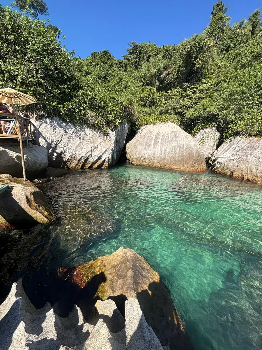 Piscina natural entre pedras claras, com a água turquesa deixando o fundo à vista.