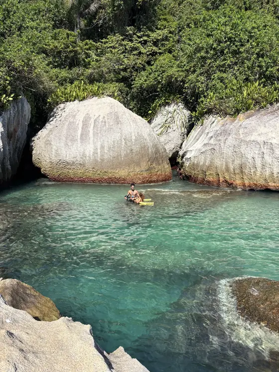 Pessoa boiando em uma piscina natural cercada de pedras.