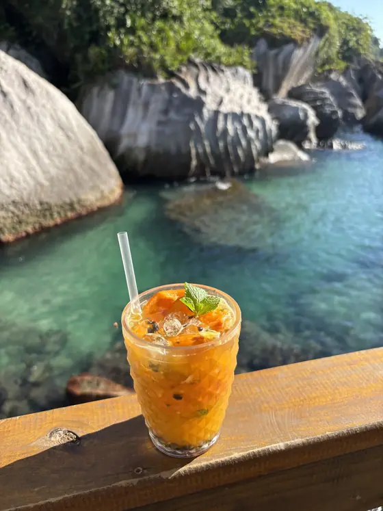 Drink de maracujá apoiado na amurada do barco, com a ilha ao fundo.