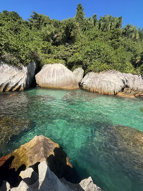 Pedras grandes e claras na borda da ilha, com a água esverdeada em primeiro plano.