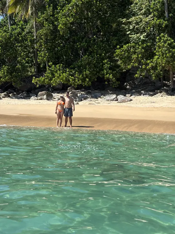 Casal na beira da praia, visto de dentro da água rasa.