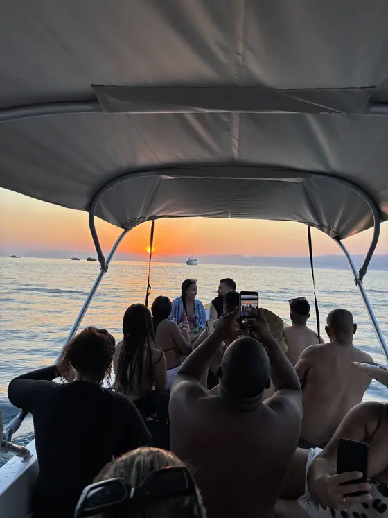 Grupo sentado no barco, sob a capota, olhando o sol nascer.